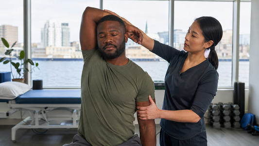A physiotherapist guides a man through an overhead arm stretch in a clinic with a harbour view behind them
